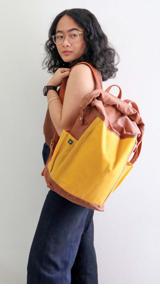 Slabtown Backpack made by Gyasti. She is posing with a mustard and field tan with chestnut leather bag she made.